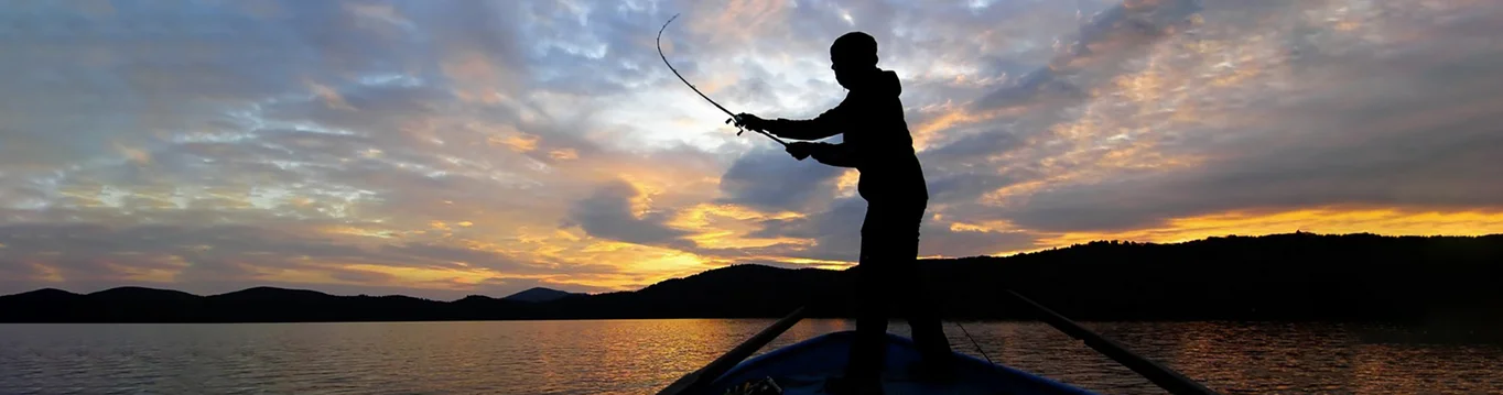Angler auf Boot wirft die Rute aus im Sonnenuntergang.